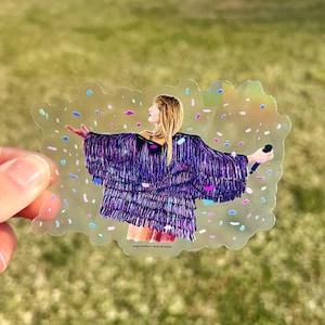 May include: A clear sticker with a holographic finish featuring a woman in a purple sequined jacket with confetti falling around her. The text "september sun studio" is at the bottom of the sticker.