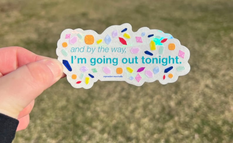 May include: A white sticker with a holographic finish and colorful confetti-like shapes. The sticker says "and by the way, I'm going out tonight."