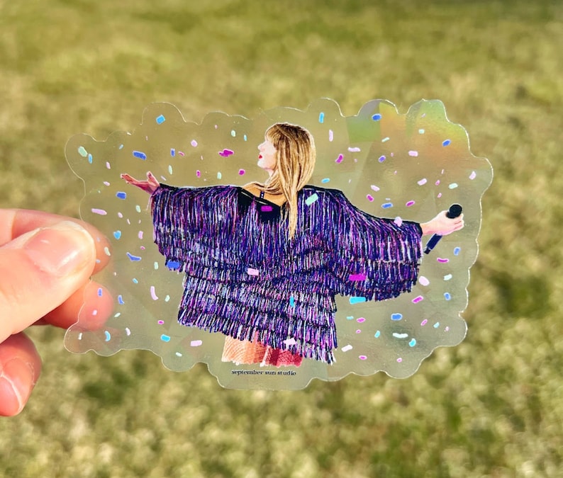 May include: A clear sticker with a colourful confetti background featuring a woman wearing a sequined purple and black jacket, holding a microphone and singing. The text "september sun studio" is at the bottom of the sticker.