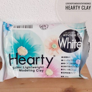 Può includere: Un pacchetto di argilla da modellare Hearty Super Lightweight di colore bianco. La confezione presenta un design floreale e il testo "White" in lettere nere. Il pacchetto è di 50g.