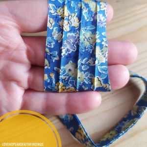 Könnte beinhalten: Ein blaues und gelbes Baumwollband mit floralem Muster. Das Band ist gefaltet und in der Mitte gefaltet. Der Text "LOVEHOPEANDFAITHFINDINGS NASTRO IN COTONE" ist in der linken unteren Ecke des Bildes sichtbar.