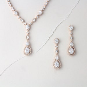May include: A rose gold necklace and earrings set with clear pear-shaped crystals. The necklace has a long pendant with multiple crystals.