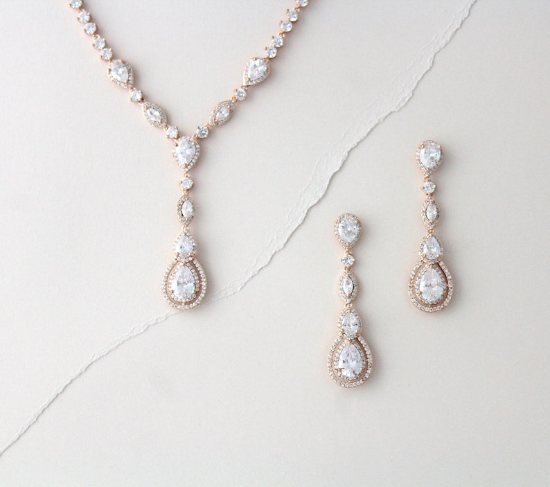 May include: A rose gold necklace and earrings set with clear pear-shaped crystals. The necklace has a long pendant with multiple crystals.