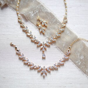 May include: A gold bridal jewellery set with a necklace, bracelet and earrings. The set features a delicate design with clear cubic zirconia stones.