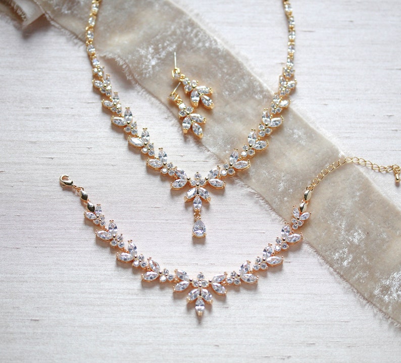 May include: A gold bridal jewellery set with a necklace, bracelet and earrings. The set features a delicate design with clear cubic zirconia stones.