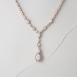 May include: A rose gold necklace with a teardrop pendant adorned with clear cubic zirconia stones. The necklace features a delicate chain with smaller cubic zirconia stones.