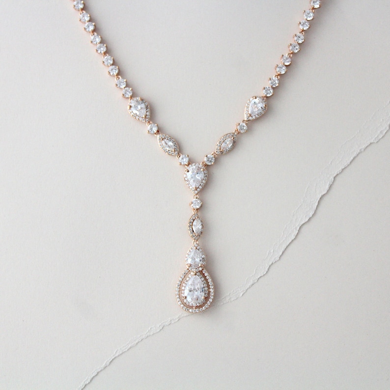 May include: A rose gold necklace with a teardrop pendant adorned with clear cubic zirconia stones. The necklace features a delicate chain with smaller cubic zirconia stones.