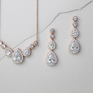 Pu&ograve; includere: Un set di collana e orecchini in oro rosa con pietre di zircone cubico a forma di pera. La collana presenta un gruppo di tre pietre, mentre gli orecchini ne hanno tre ciascuna, a cascata.