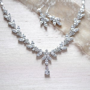 May include: A silver necklace and earrings set with a teardrop pendant and a delicate leaf design. The jewellery is made with clear cubic zirconia stones.