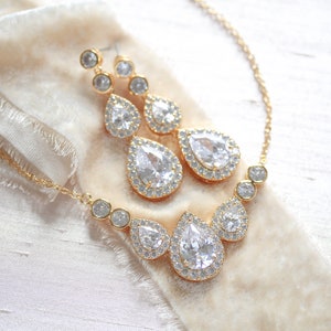 Pu&ograve; includere: Un set di collana e orecchini in oro con cristalli a forma di goccia d'acqua circondati da cristalli pi&ugrave; piccoli.
