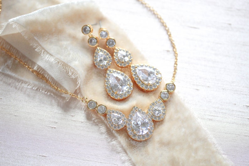 Pu&ograve; includere: Un set di collana e orecchini in oro con cristalli a forma di goccia d'acqua circondati da cristalli pi&ugrave; piccoli.