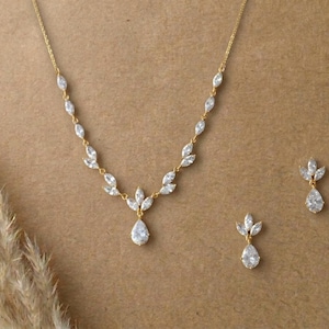 Gold bridal necklace and earrings set with marquise cubic zirconia leaves and pear-shaped CZ drops displayed on a neutral background for the Exquisite Bride.