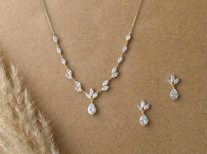 Gold bridal necklace and earrings set with marquise cubic zirconia leaves and pear-shaped CZ drops displayed on a neutral background for the Exquisite Bride.