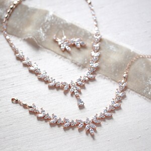 May include: A rose gold bridal jewellery set with a necklace, bracelet and earrings. The set features a delicate leaf design with clear cubic zirconia stones.