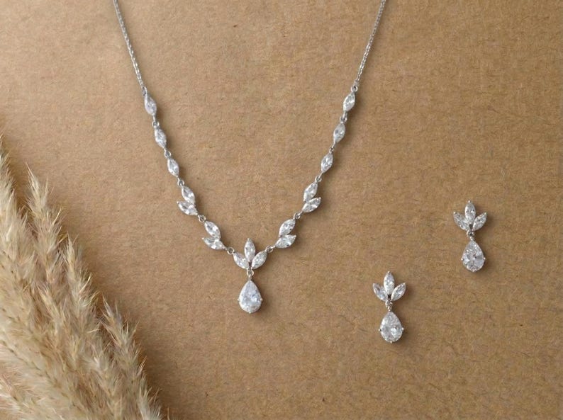 Silver bridal necklace and earrings set featuring marquise cubic zirconia leaves and pear-shaped CZ drops displayed on a neutral background for the Exquisite Bride.
