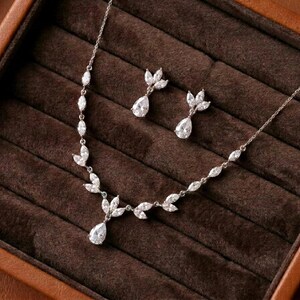 Silver bridal necklace and earrings set with cubic zirconia marquise leaves and pear-shaped CZ drops displayed in a luxury jewelry box for the Exquisite Bride.