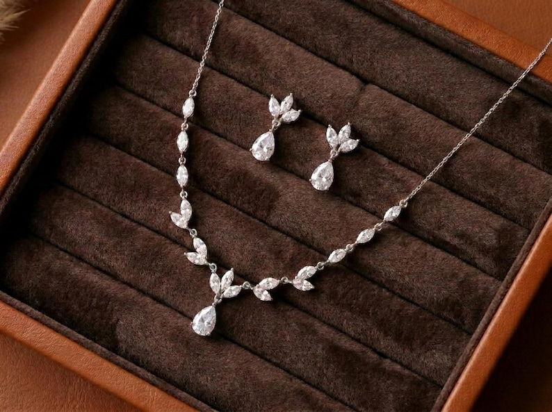 Silver bridal necklace and earrings set with cubic zirconia marquise leaves and pear-shaped CZ drops displayed in a luxury jewelry box for the Exquisite Bride.