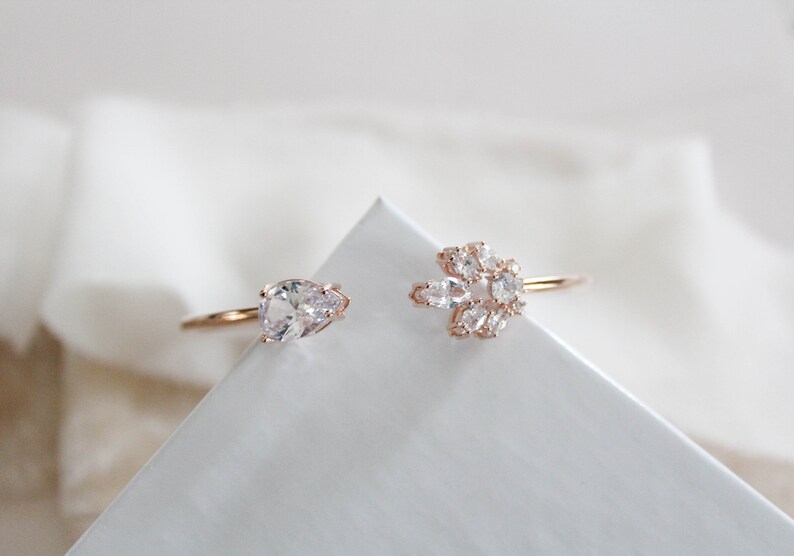 K&ouml;nnte beinhalten: Zwei goldene Ringe mit klaren Zirkonia-Steinen. Ein Ring hat einen einzelnen birnenf&ouml;rmigen Stein, der andere hat eine Gruppe kleinerer Steine.