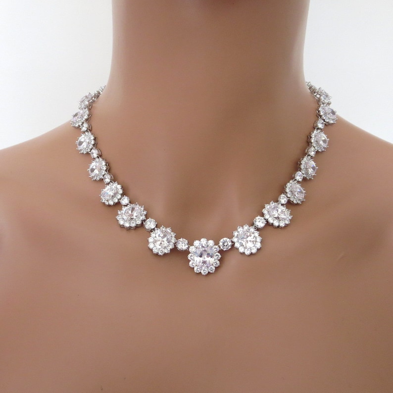 May include: A silver necklace with a row of large, clear, round rhinestones. The rhinestones are set in a cluster of smaller rhinestones.