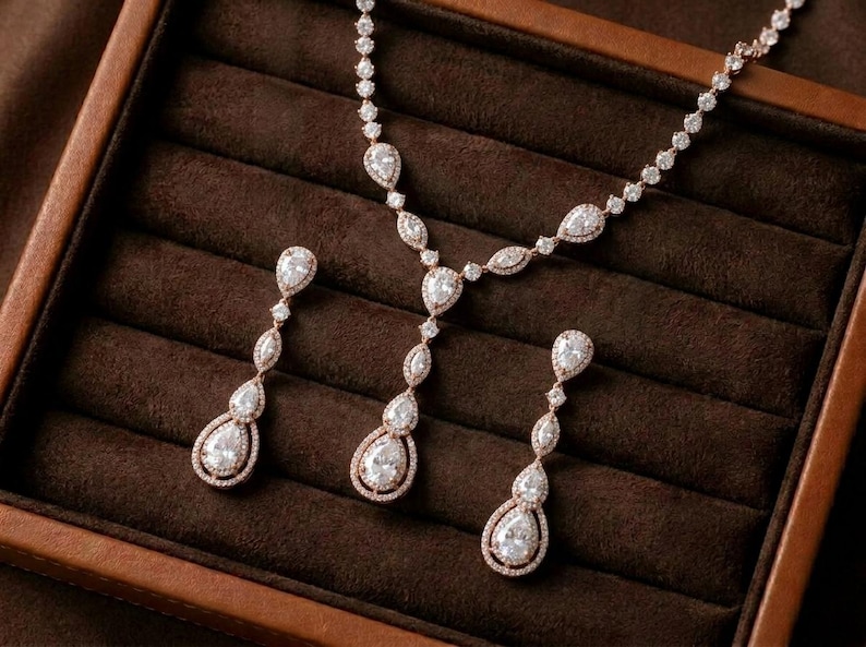Rose gold cubic zirconia bridal necklace and matching drop earrings displayed on a luxury brown jewelry tray for bridal jewelry.