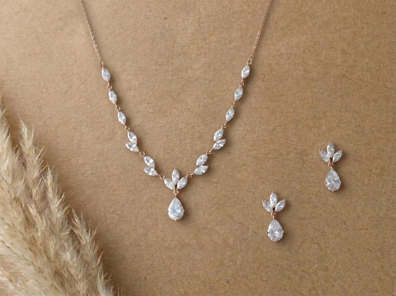 Rose gold bridal necklace and earrings set with marquise cubic zirconia leaves and pear-shaped CZ drops displayed on a neutral background for the Exquisite Bride.