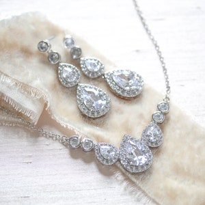 Pu&ograve; includere: Un set di collana e orecchini in argento con cristalli a forma di goccia d'acqua circondati da cristalli pi&ugrave; piccoli.