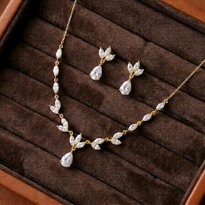 Gold bridal necklace and earrings set featuring sparkling cubic zirconia marquise leaves with pear-shaped CZ drops displayed in a luxury jewelry box for the Exquisite Bride.