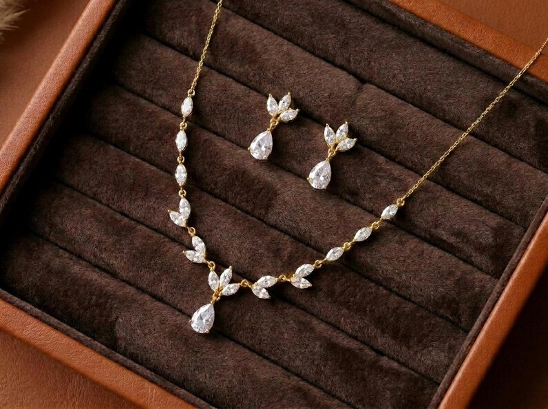 Gold bridal necklace and earrings set featuring sparkling cubic zirconia marquise leaves with pear-shaped CZ drops displayed in a luxury jewelry box for the Exquisite Bride.