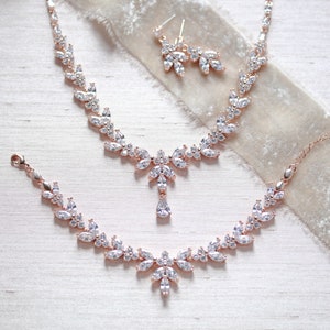 May include: A rose gold bridal jewellery set with a necklace, bracelet and earrings. The set features a delicate design with clear cubic zirconia stones.