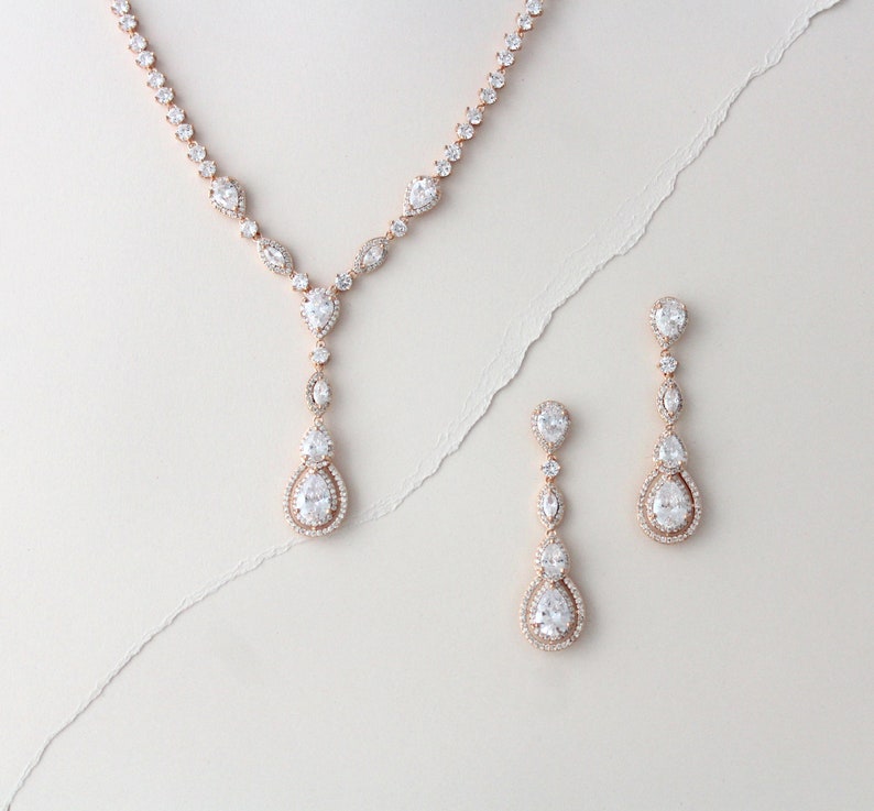 May include: A rose gold necklace and earrings set with pear-shaped clear crystals. The necklace has a long pendant with multiple crystals.