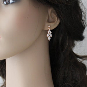 May include: Rose gold dangle earrings with clear crystal stones in a leaf design.