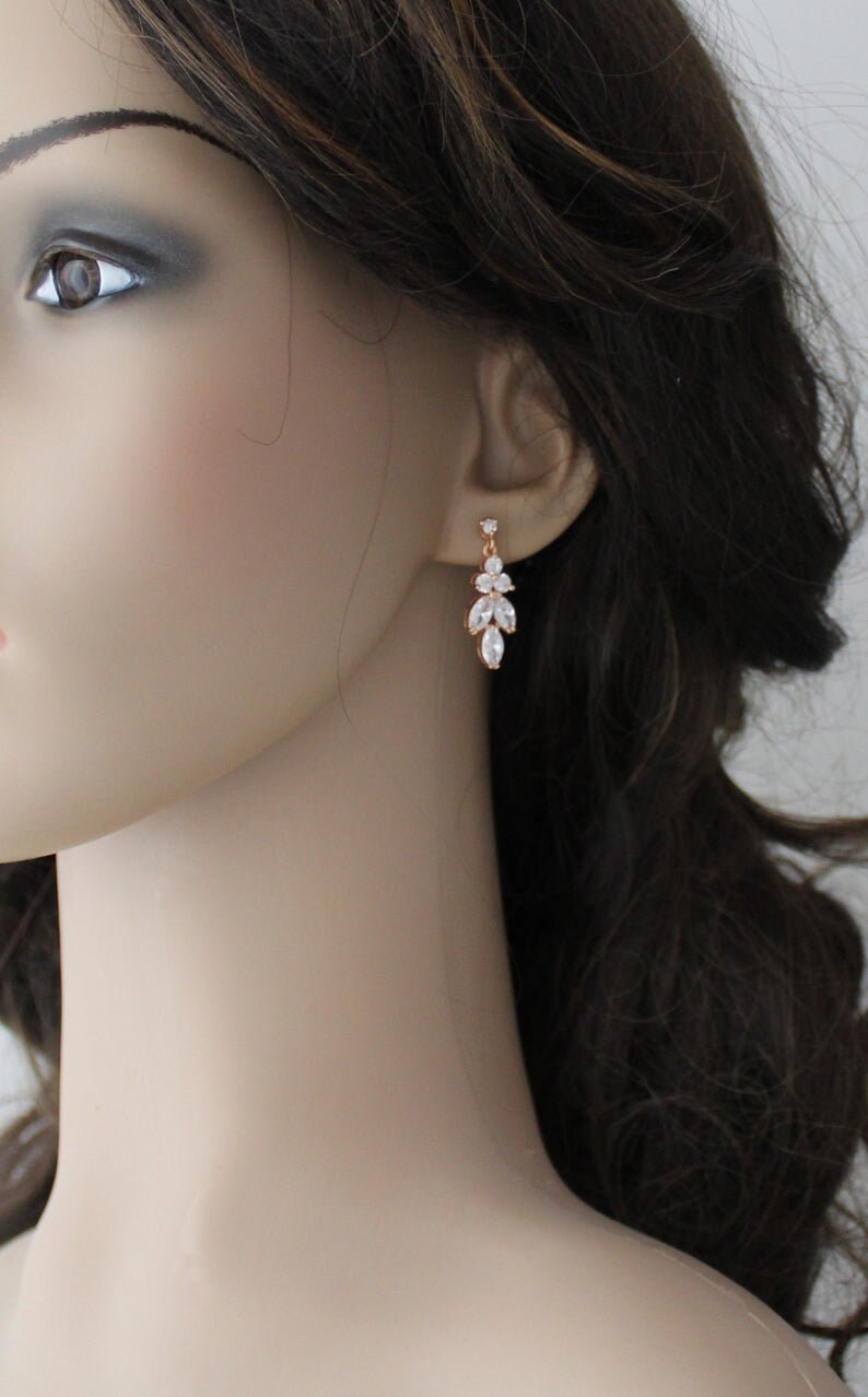 May include: Rose gold dangle earrings with clear crystal stones in a leaf design.