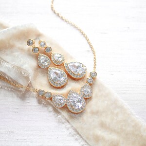 Pu&ograve; includere: Un set di collana e orecchini in oro con cristalli trasparenti a forma di goccia d'acqua circondati da cristalli pi&ugrave; piccoli.