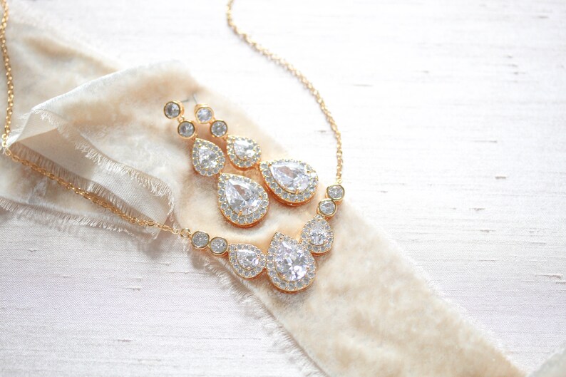 Pu&ograve; includere: Un set di collana e orecchini in oro con cristalli trasparenti a forma di goccia d'acqua circondati da cristalli pi&ugrave; piccoli.
