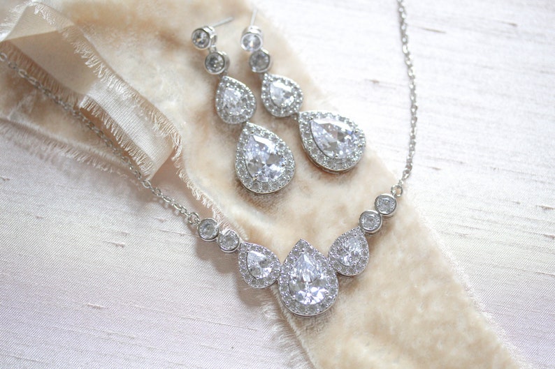 Pu&ograve; includere: Un set di collana e orecchini in argento con accenti di cristallo a forma di goccia. La collana presenta una fila di cristalli pi&ugrave; piccoli e tre cristalli pi&ugrave; grandi a forma di goccia.