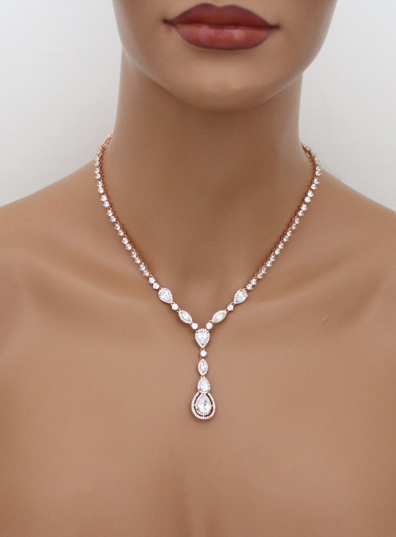 May include: A rose gold necklace with a teardrop pendant. The necklace is made of cubic zirconia stones and has a delicate design.