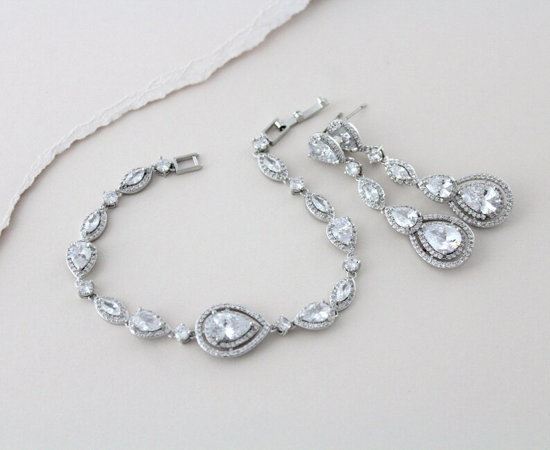 以下が含まれることがあります： 梨型のクリアなキュービックジルコニアが施されたシルバーのブレスレットとイヤリングのセットです。