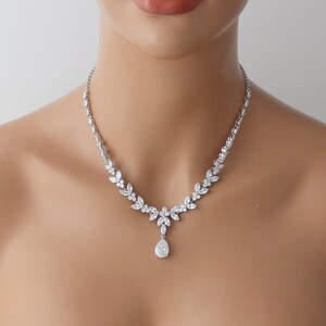 May include: A silver necklace with a teardrop pendant and a delicate, leaf-shaped design. The necklace is made of cubic zirconia stones and is perfect for a wedding or special occasion.