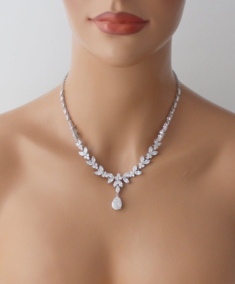 May include: A silver necklace with a teardrop pendant and a delicate, leaf-shaped design. The necklace is made of cubic zirconia stones and is perfect for a wedding or special occasion.
