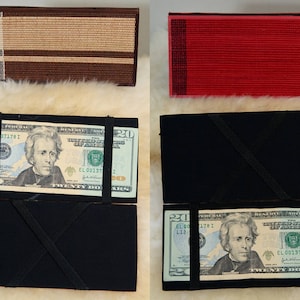 May include: A black wallet with two twenty dollar bills inside. The bills are folded in half and secured with a black strap. The wallet is made of a soft, black fabric. The bills feature the portrait of Andrew Jackson.