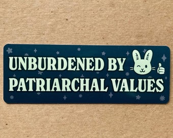 May include: A rectangular sticker with the text "UNBURDENED BY PATRIARCHAL VALUES" in white, on a dark teal background. A winking bunny with a thumbs-up is on the right. The sticker is next to a dime.