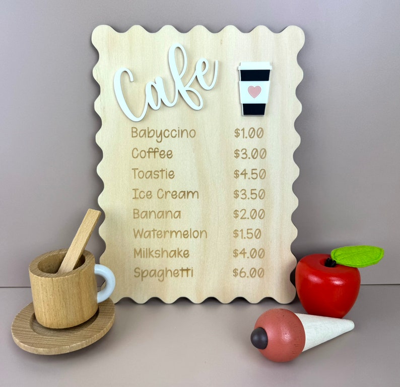 May include: A wooden sign with a cafe menu, featuring items like babyccino, coffee, toastie, ice cream, banana, watermelon, milkshake, and spaghetti. The prices are listed next to each item. The sign is decorated with a wooden cup and a red apple.