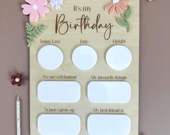 May include: A wooden birthday board with a white background and a brown inscription that reads "It's my Birthday". The board has eight blank spaces for writing or drawing, including spaces for "Today I am", "Date", "Height", "We are celebrating", "My favorite things", "When I grow up", and "My best friend is". The board is decorated with colorful flowers.