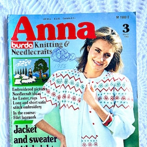 May include: A vintage magazine cover for "Anna Burda Knitting & Needlecrafts" from March 1982. The cover features a woman wearing a white cardigan and sweater with a red and green pattern. The magazine includes knitting and needlecraft ideas.