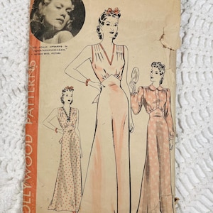 Op de afbeelding: Een vintage Hollywood Patterns naaipatroon-envelop D-9889, maat 14, met illustraties van drie vloerlange jurken. De beige papieren envelop bevat een zwart-wit portret van Jane Wyman, tekst en een prijs van 15 cent.