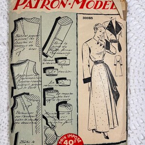 May include: A vintage sewing pattern envelope labeled Patron-Modèle 30085 featuring a black and white illustration of a long-sleeved robe with a dark collar and cuffs. The paper envelope includes technical diagrams, French text instructions, and a red circular price sticker.