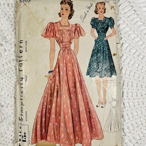 May include: A vintage Simplicity pattern envelope 3303 featuring illustrations of two dresses with square necklines and puff sleeves. One dress is floor-length and pink with a white floral print, while the other is knee-length and teal with a floral pattern.