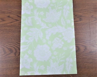 May include: A light green sheet of wrapping paper with a white floral pattern. The pattern features stylized flowers, leaves, and stems.