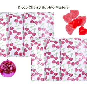 May include: Two white bubble mailers with a repeating pattern of red cherries on a white background. The mailers are shown next to a pink disco ball and red heart-shaped candies.