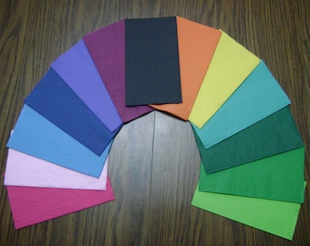May include: A fan-shaped arrangement of 12 different colored paper squares. The colors are pink, red, light blue, dark blue, purple, maroon, black, orange, yellow, light green, dark green, and lime green.